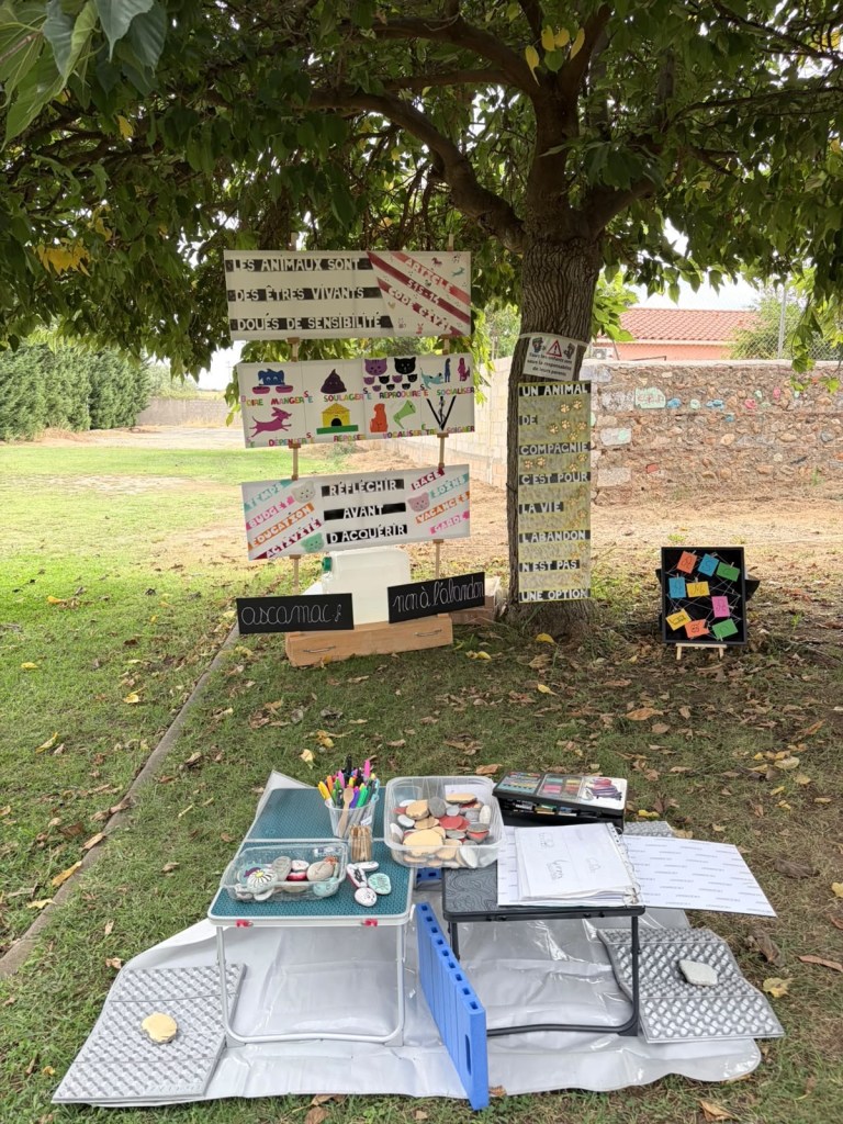 Stand de sensibilisation d’ASCaMaC installé sous un arbre, avec panneaux sur les besoins des animaux et activités créatives.